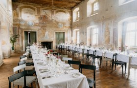 Elegant dining room in a castle with long, laid tables and murals.