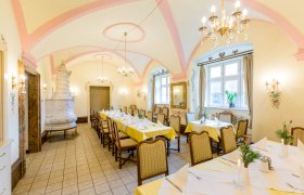 Elegant dining room with laid tables, chandeliers and tiled stove.