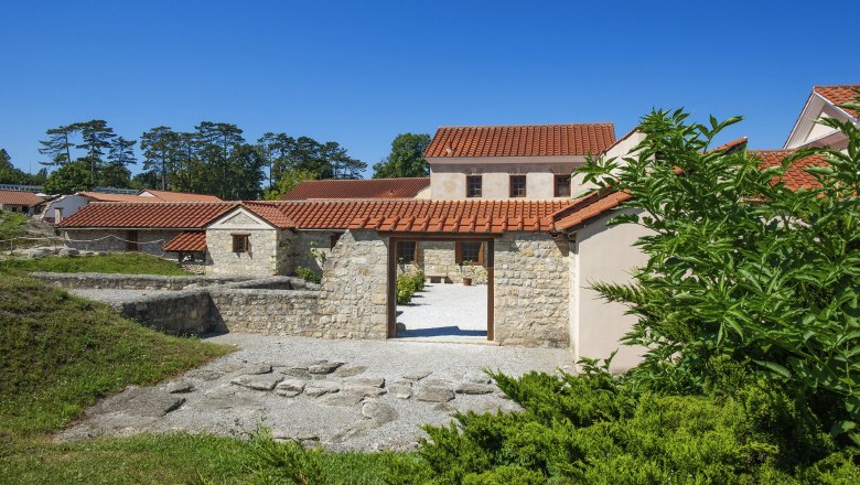 Reconstructed Roman buildings in Carnuntum with red tiled roofs and stone walls, surrounded by green vegetation.