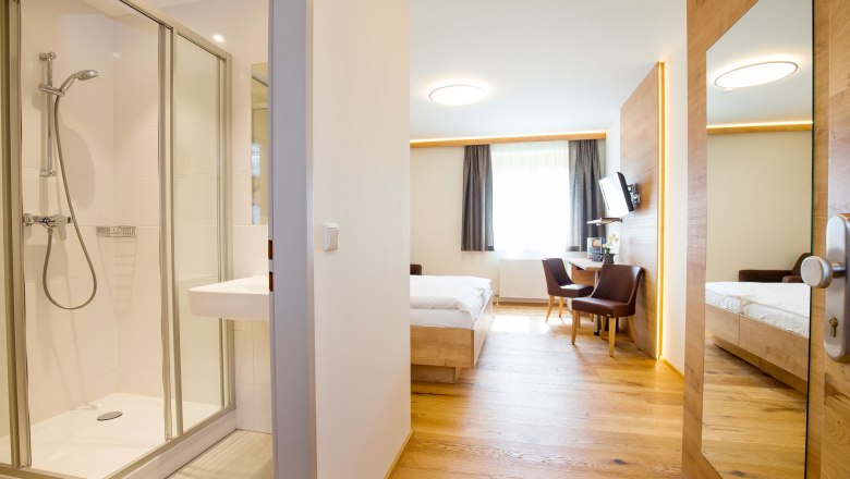 Modern hotel room with bathroom, bed, desk and chairs.