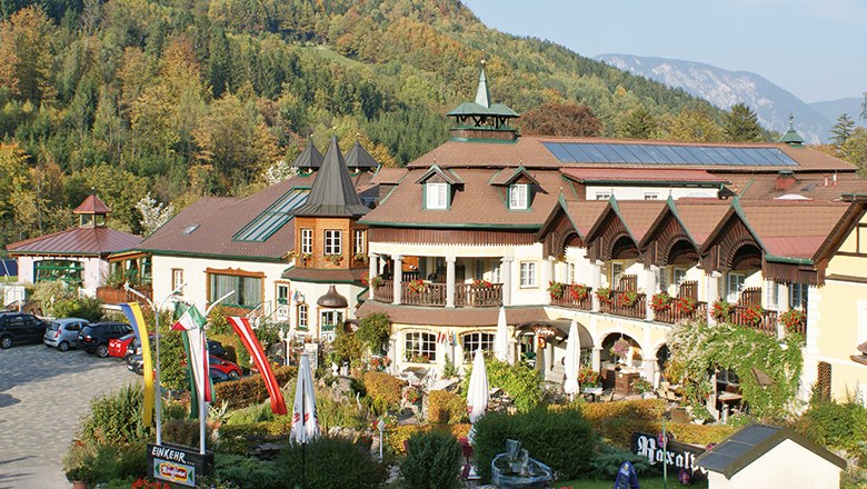 A traditional hotel in a mountainous landscape with colorful flags and parasols in the garden.