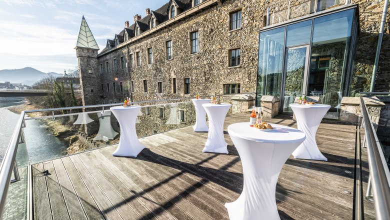 Terrace with bar tables in front of a historic building with a glass façade.