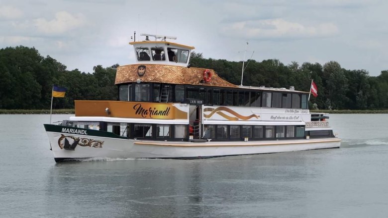 An excursion boat named MS Mariandl sails on a river surrounded by trees. It carries the flags of Ukraine and Austria.