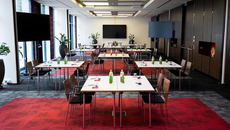 A modern conference room with red carpets, white tables and chairs, equipped with beverages and writing supplies.