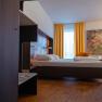 Modern hotel room with bed, yellow curtains and colorful painting on the wall.