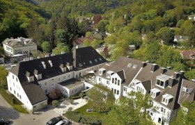 Aerial view of a large building complex surrounded by green trees and hills.