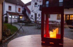 Lantern with a burning candle on a wooden table in the courtyard of a country hotel.