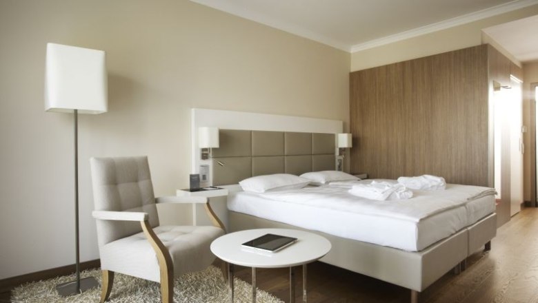 Modern hotel room with double bed, armchair, table and floor lamp.