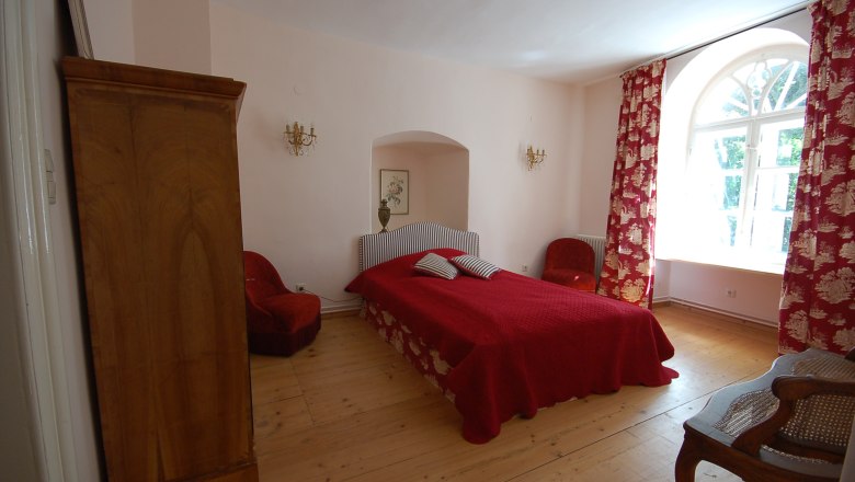 A cozy bedroom with a red bed, red curtains and wooden furniture.