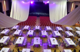 An event room with tables and chairs, purple lighting and a stage in the background.