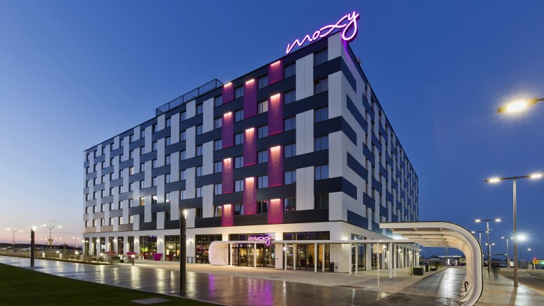 Exterior view of the Moxy Vienna Airport Hotel at dusk with illuminated lettering.