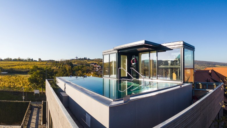 Rooftop pool with glass walls on a modern building surrounded by countryside.