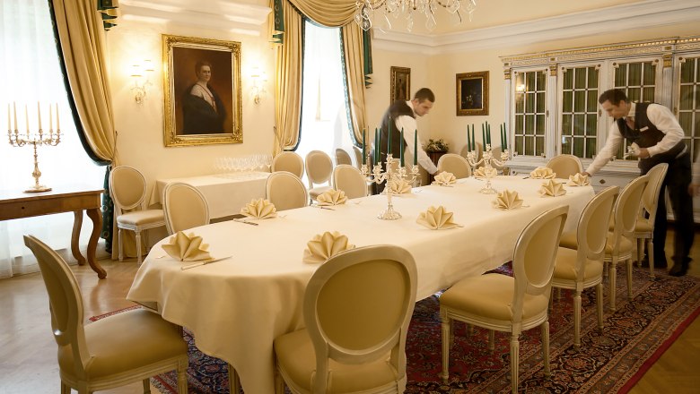 Elegant dining room with laid table, candlesticks and two waiters.