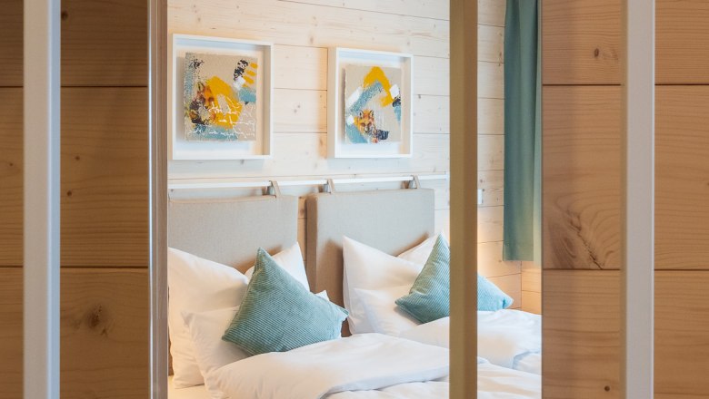 A cozy double room with wood paneling, two beds, blue pillows and modern art on the wall.