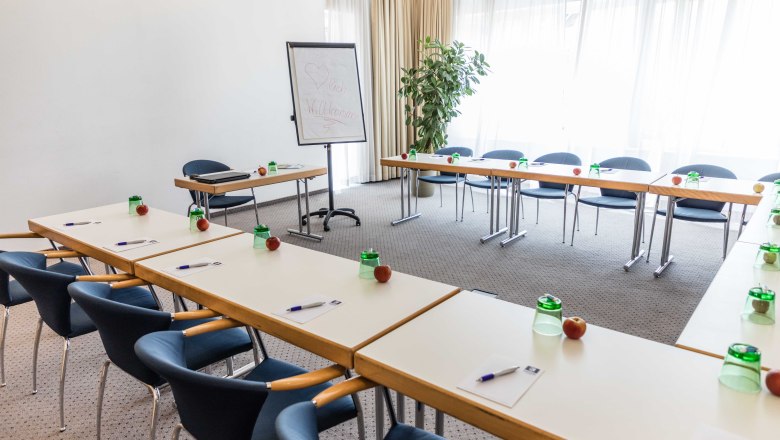 Conference room with U-shaped tables, chairs, flipchart and writing materials.