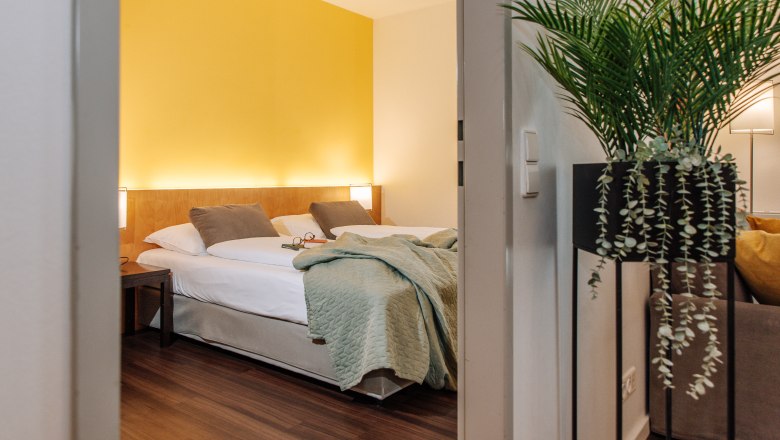 Hotel room with yellow wall, double bed and plant in the foreground.
