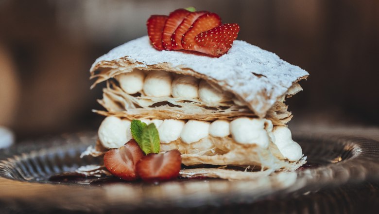A cream slice with puff pastry, cream and strawberries on a plate.