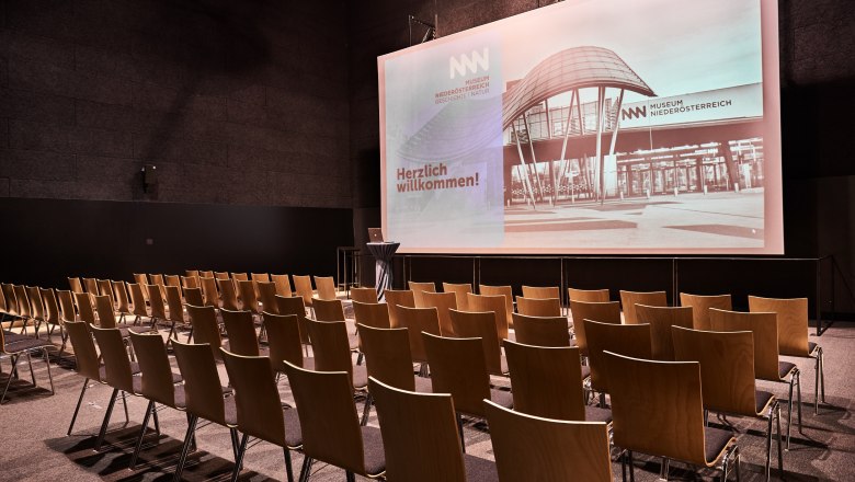 Empty cinema hall in the Museum Nieder&ouml;sterreich with rows of chairs and a large screen.