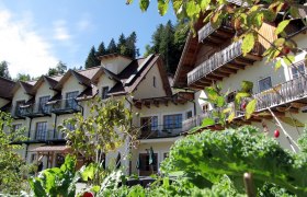 An alpine-style building with balconies, surrounded by lush greenery and plants.