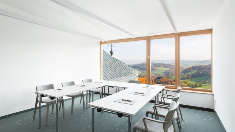 Seminar room with tables and chairs, large window overlooking the countryside.