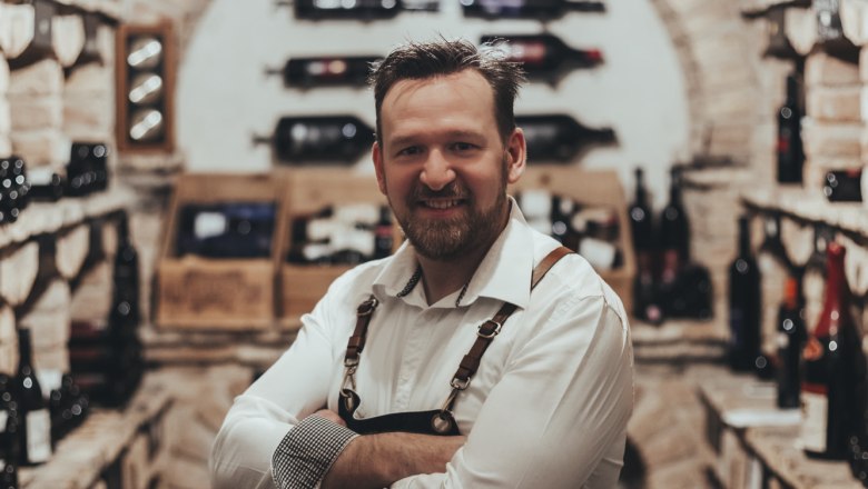 A man in a wine cellar with shelves full of wine bottles.