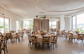 Elegant function room with round tables, chairs and floral decorations.