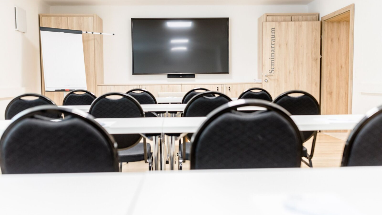 A modern seminar room with chairs, tables, a large screen and a flipchart.