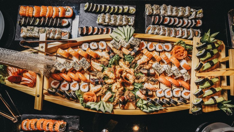 A rich sushi buffet on a wooden tray, decorated with different types of sushi and sashimi, cucumber and ginger.