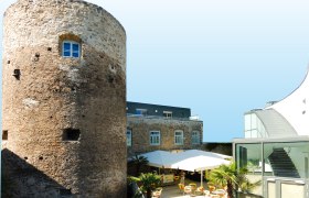 Historic tower next to modern building with terrace and parasols.