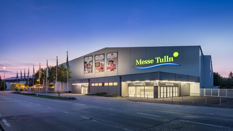 Exterior view of Messe Tulln at dusk with illuminated entrance and flags.