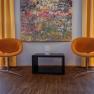 Two orange chairs in front of a colorful painting and yellow curtains.