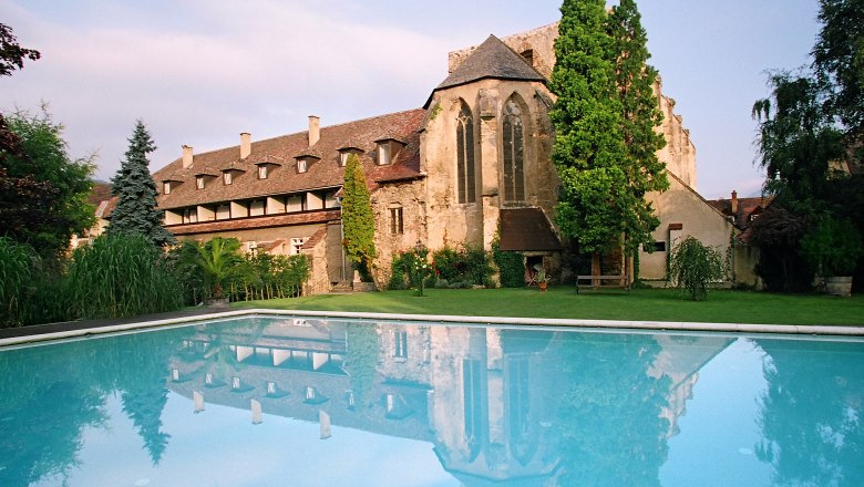 Historic building with pool in the foreground, surrounded by trees and garden.