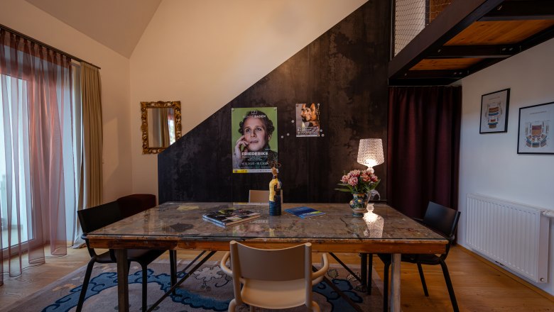 A stylishly furnished room with a table, chairs, a lamp and posters on the wall.