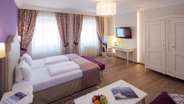 Elegant hotel room with double bed, desk, TV and fruit plate.