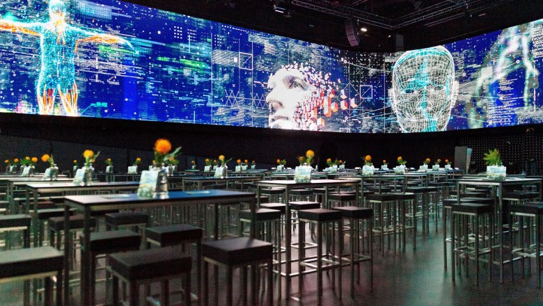 A modern showroom with digital projections and tables with flowers.