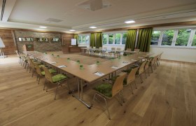 Seminar room with U-shaped table arrangement, green chairs and large windows.