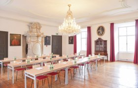 Elegant seminar room with chandelier, wooden floor and portraits on the walls.