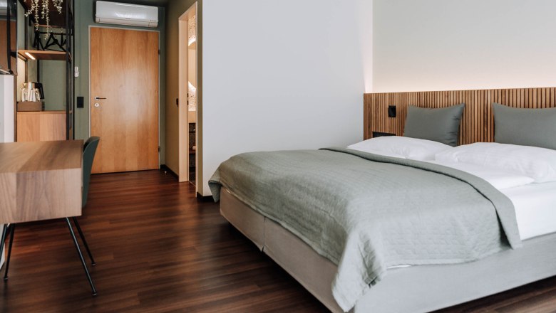 Modern hotel room with double bed, wooden floor and desk.