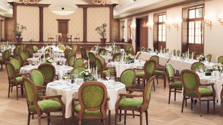 Elegant ballroom with laid tables and green chairs in Schloss Thalheim.