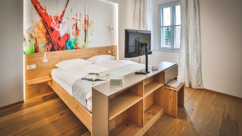 A modern hotel room with a double bed, an abstract artwork on the wall, and a TV on a shelf.