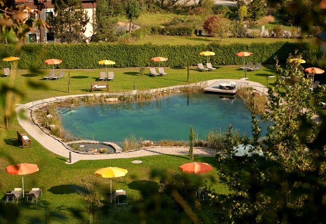 A natural swimming pond with sun loungers and colorful parasols on a green meadow.