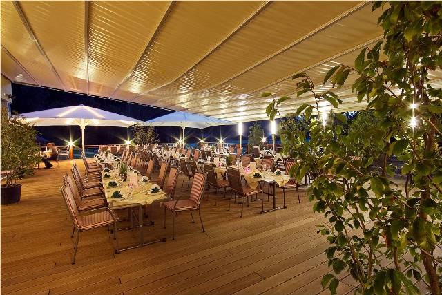 A festively decorated terrace with tables and chairs under a large sunshade at night.