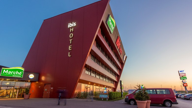 Modern hotel building with sloping fa&ccedil;ade and illuminated lettering 'ibis HOTEL'.