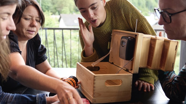 Four people work together on a wooden box with a combination lock.