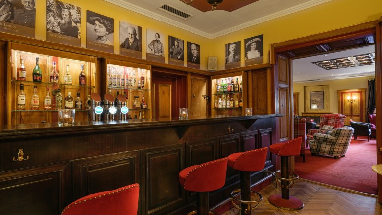 Interior view of a stylish bar with wooden counter, red bar stools and pictures on the wall.