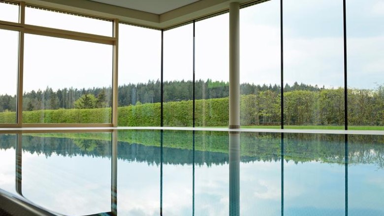Indoor pool with large windows and views of the forest and hedges.