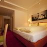 A cozy hotel room with a double bed, desk and mural. Warm lighting and red carpets create an inviting atmosphere.
