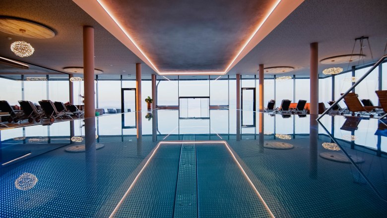 Interior view of an infinity pool with sun loungers and large windows.