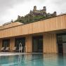 Modern outdoor pool with wooden cladding and castle ruins in the background.