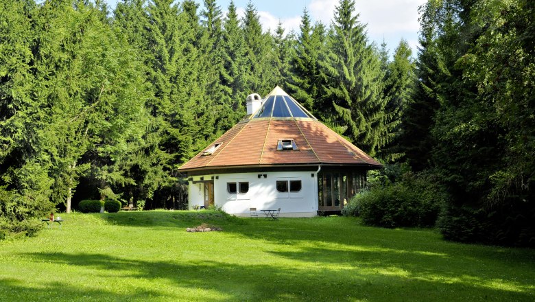 A round house with a pyramid roof in the middle of a forest.